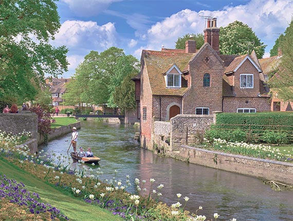 Westgate Gardens in Canterbury, with someone punting a boat down the River Stour and greenery and flowers in the park.