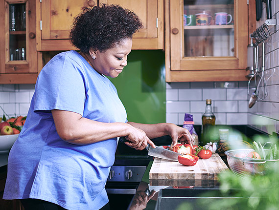A woman standing in her kitchen, preparing a meal by chopping vegetables