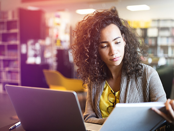 A woman working at a laptop in the library during the evening.