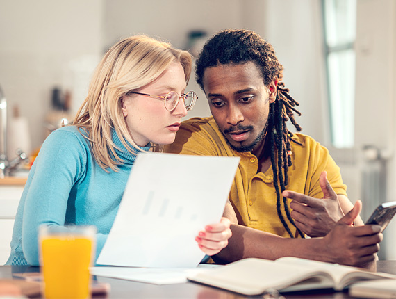 A worried looking couple looking over bills in their kitchen.