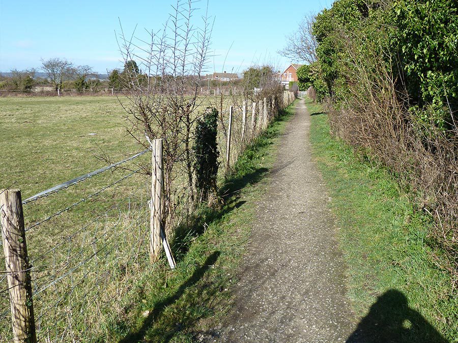 A narrow and uneven country footpath, bordered by a wonky fence.