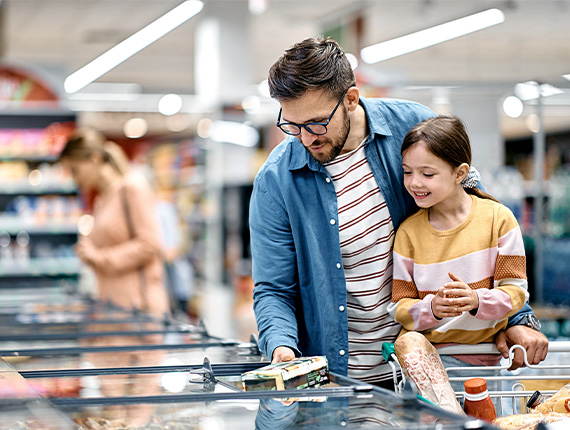 A father and his young daughter choosing food from the freezer compartment of a supermarket.