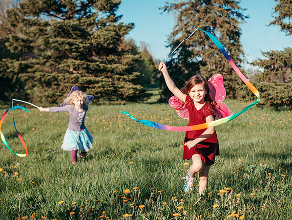 wo primary school aged girls running through a meadow twirling rainbow coloured ribbons