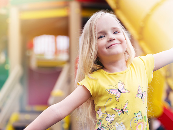 Young girl wearing yellow butterfly t-shirt runs through a play area smiling