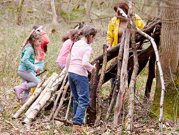 Four primary aged children building a den using tree branches supported by a park ranger